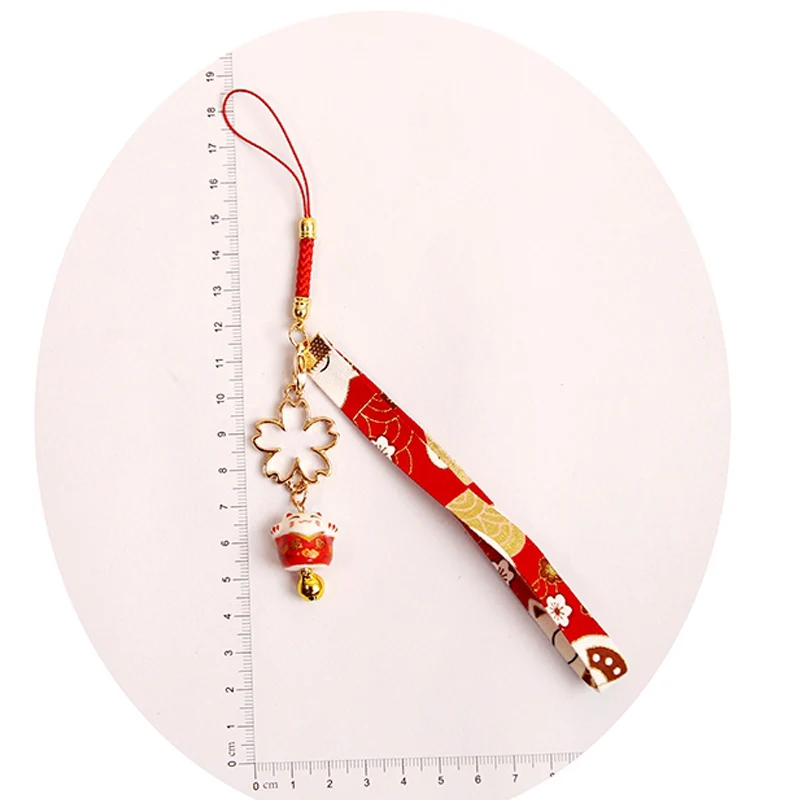 Японский брелок «Счастливый кот» цвета конфетки с колокольчиком и подвеской в виде вишневого цветка на верёвке для флешки или рюкзака. Аксессуары для ювелирных изделий.