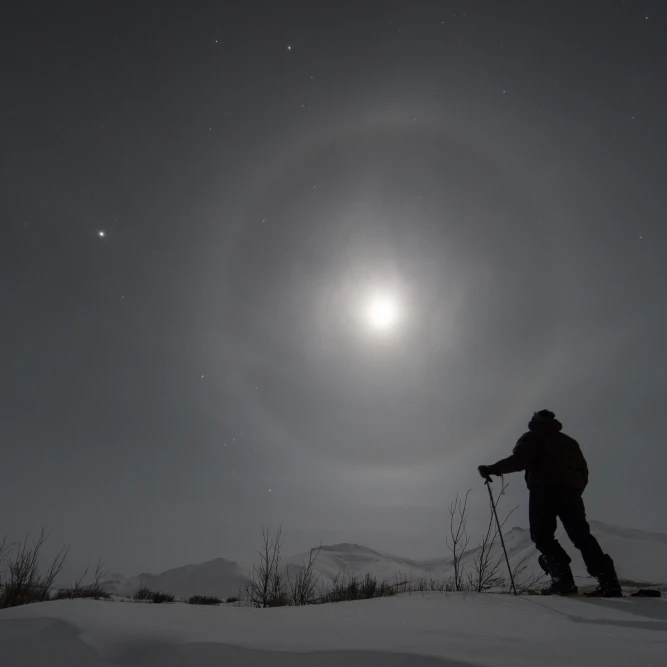 Человек снегоступы вдоль Dempster Highway под луной светящиеся с кольцами Yukon Канада