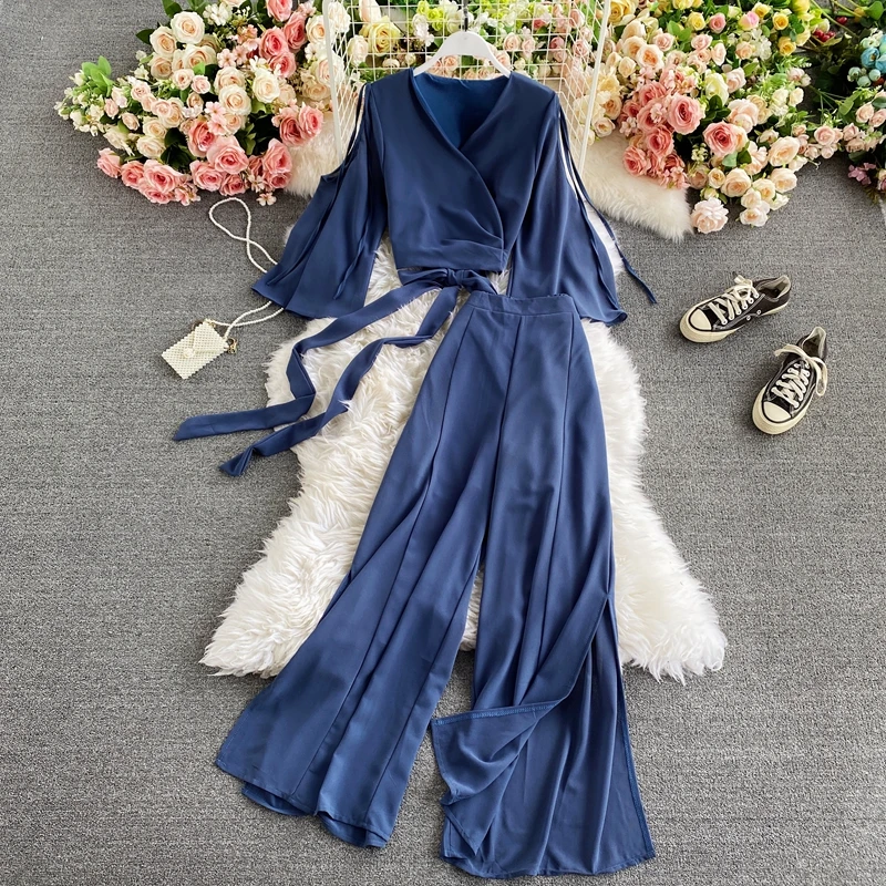 

Стильный комплект из двух предметов: топ с коротким Расклешенным рукавом и V-образным вырезом на завязках и широкие брюки с высокой талией и ...