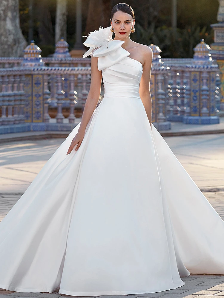 Атласное свадебное платье белого цвета на одно плечо с перьями и большим бантом